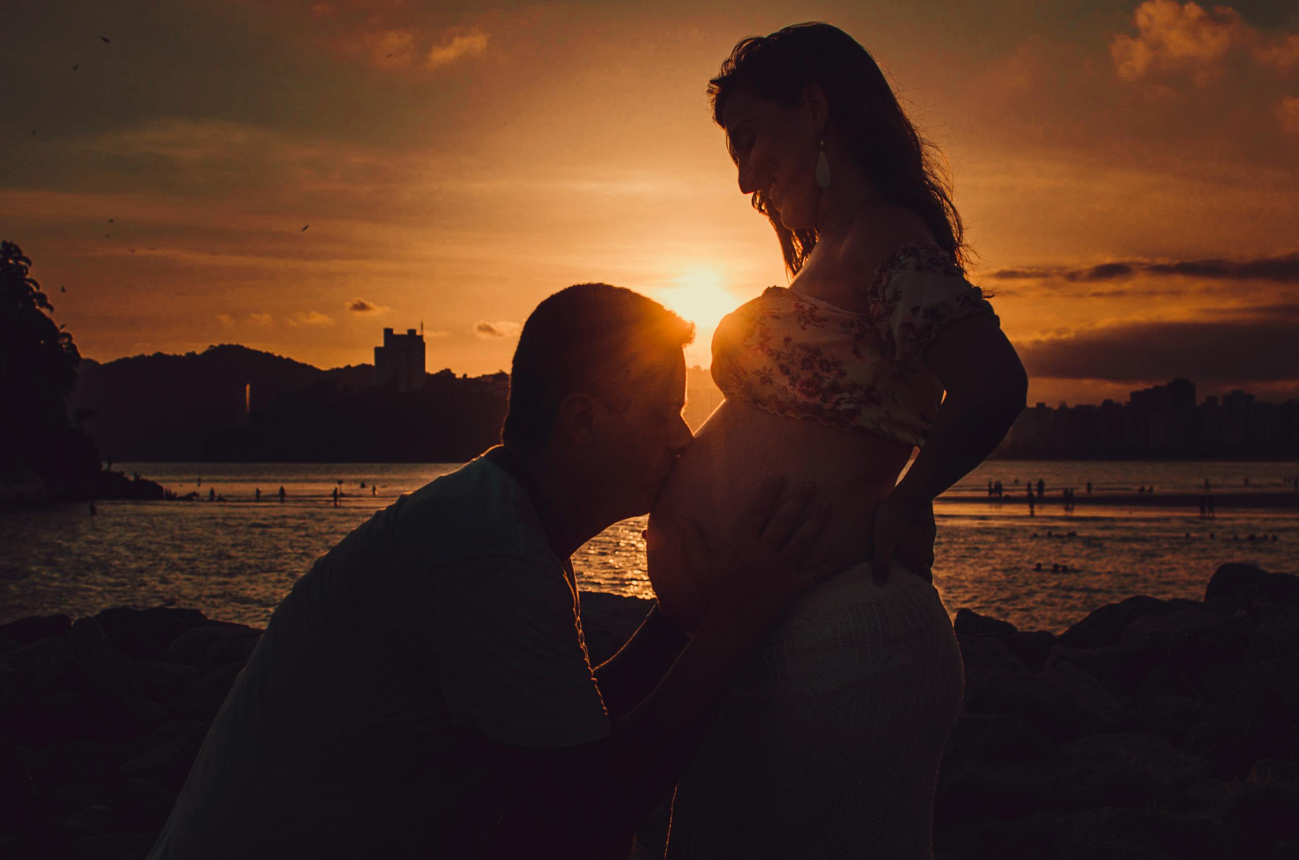 Silhouette of a loving couple at the beach during sunset, embracing pregnancy.